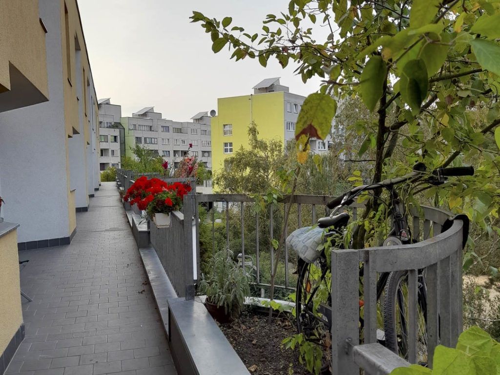 Foto eines durchgehenden "Balkons", von dem die oberen Wohnungen wie von einer Starße aus betreten werden können. Im begrünten Erker ist ein Fahrrad angeschlossen. So vorgefunden in der High-Deck-Siedlung in Berlin-Neukölln