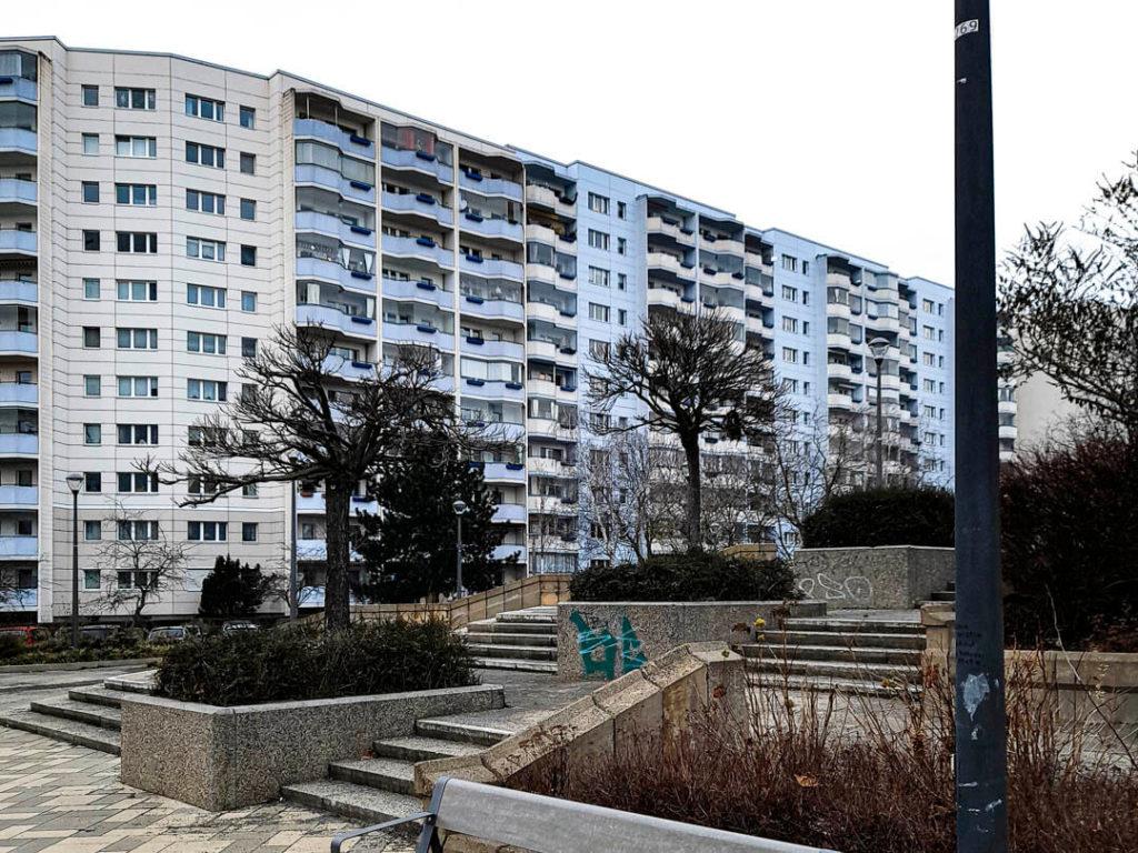 Foto eines blau-weißen Gebäuderiegels, davor ein Platz mit Steintreppen und kahlen Bäumen (is halt Winter, ne), Marzahner Promenade